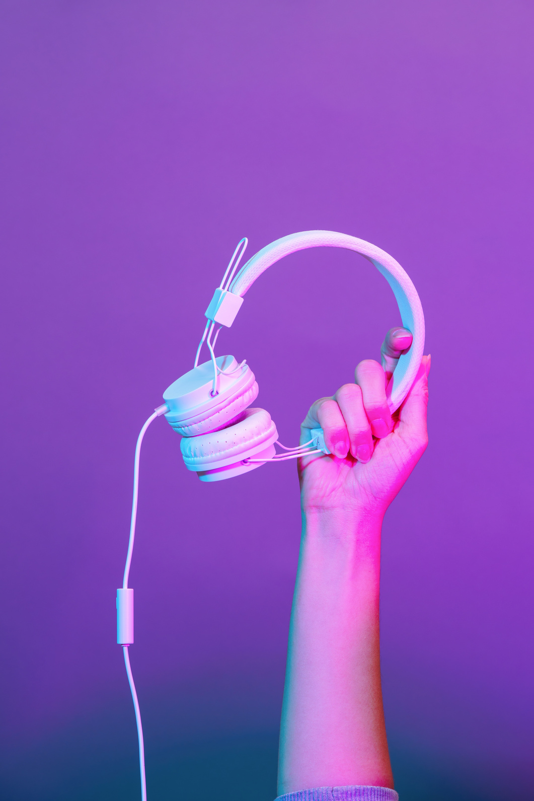 Hands with white headphones on violet background.